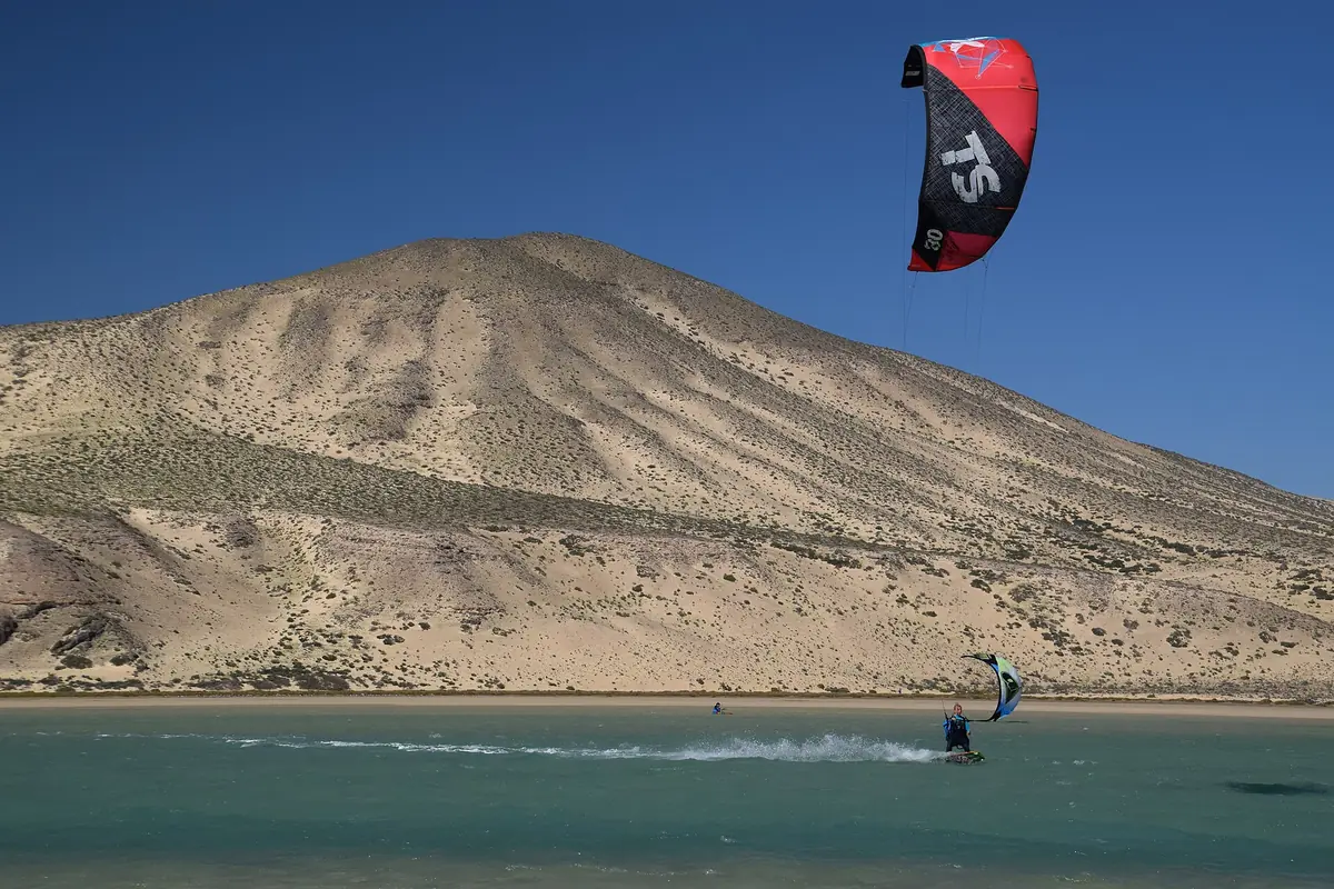 Una persona haciendo kitesurf en la laguna de Sotavento, con una montaña de arena al fondo