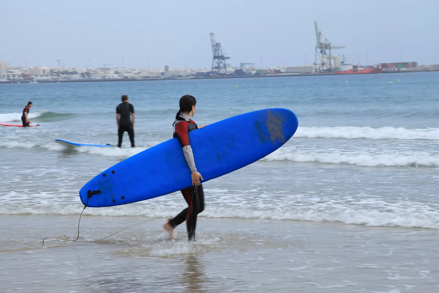 Una persona sale del agua con una tabla de surf azul en Playa Blanca, Puerto del Rosario
