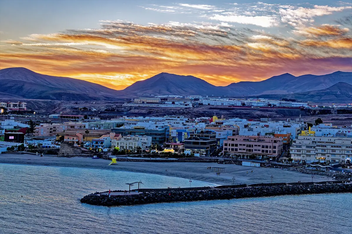Vista de Puerto del Rosario al atardecer, con la playa, el dique y las montañas al fondo