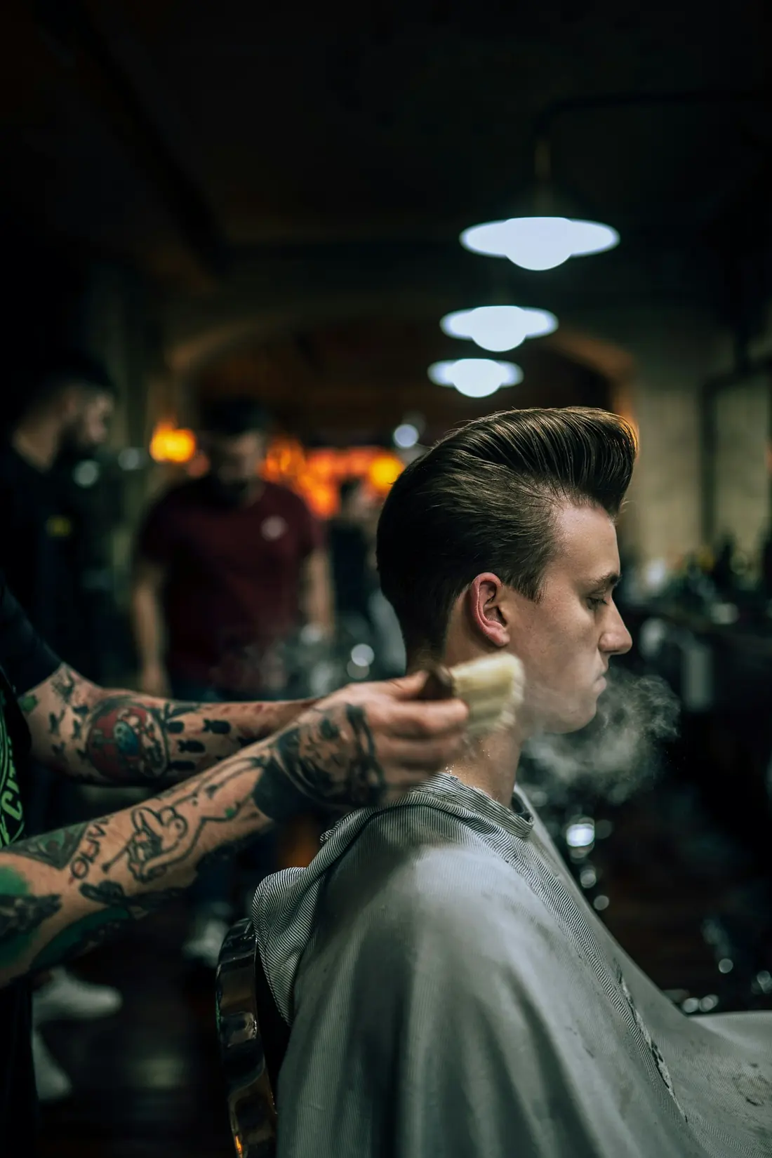 Barbero tatuado aplicando espuma en la nuca de un cliente