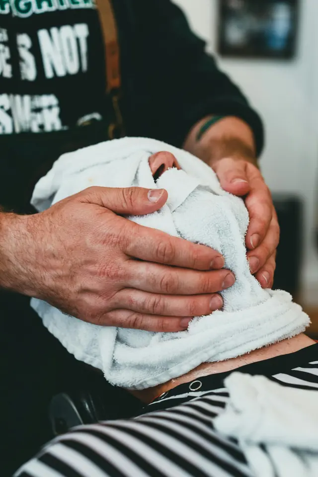 Barbero colocando una toalla caliente sobre la cara de un cliente
