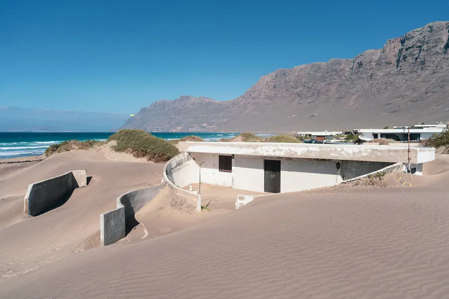Casas blancas junto a una playa de arena con montañas al fondo